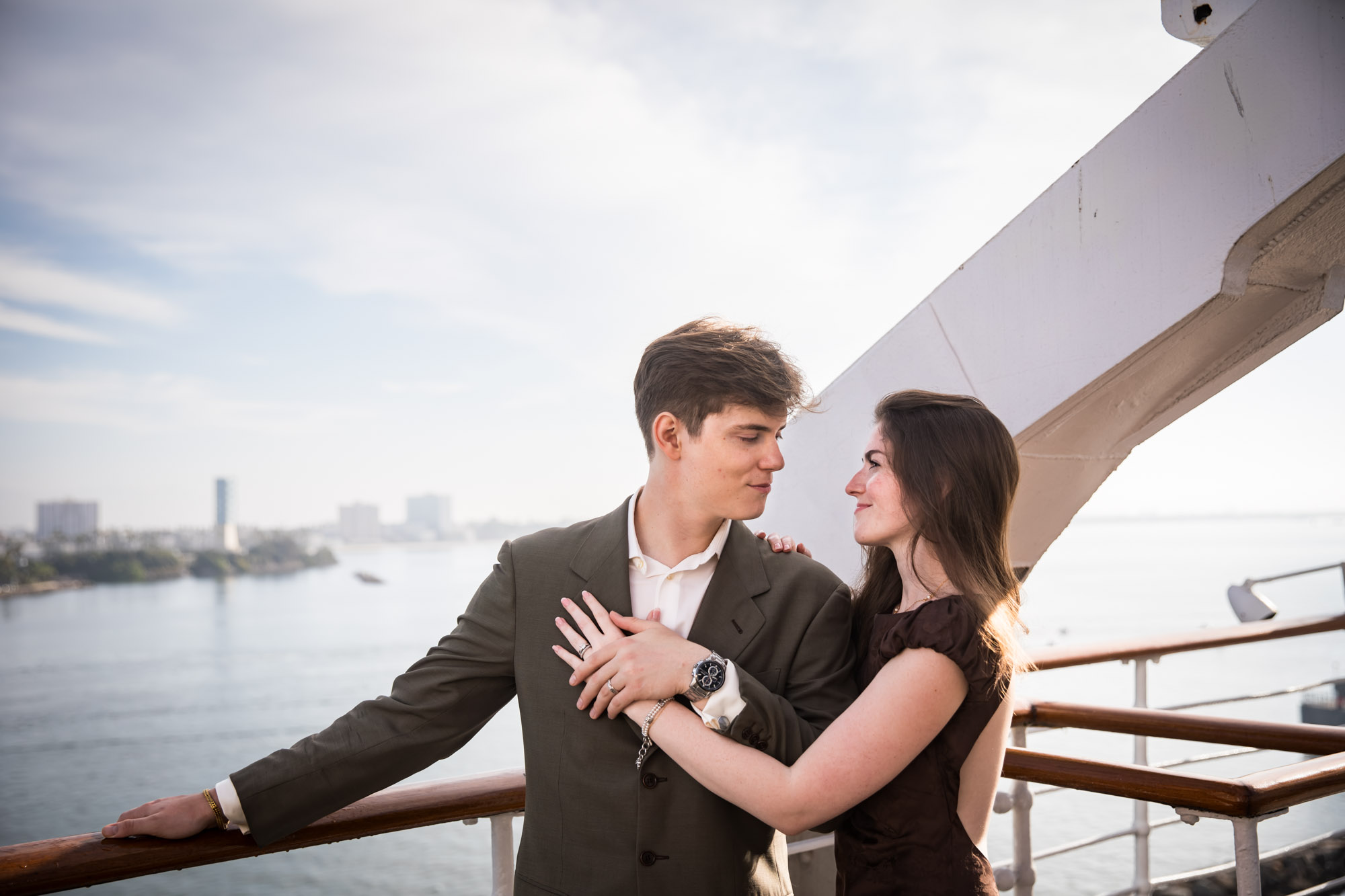 Man and woman gazing at each other with the Long Beach harbor behind them, during their Queen Mary photo shoot