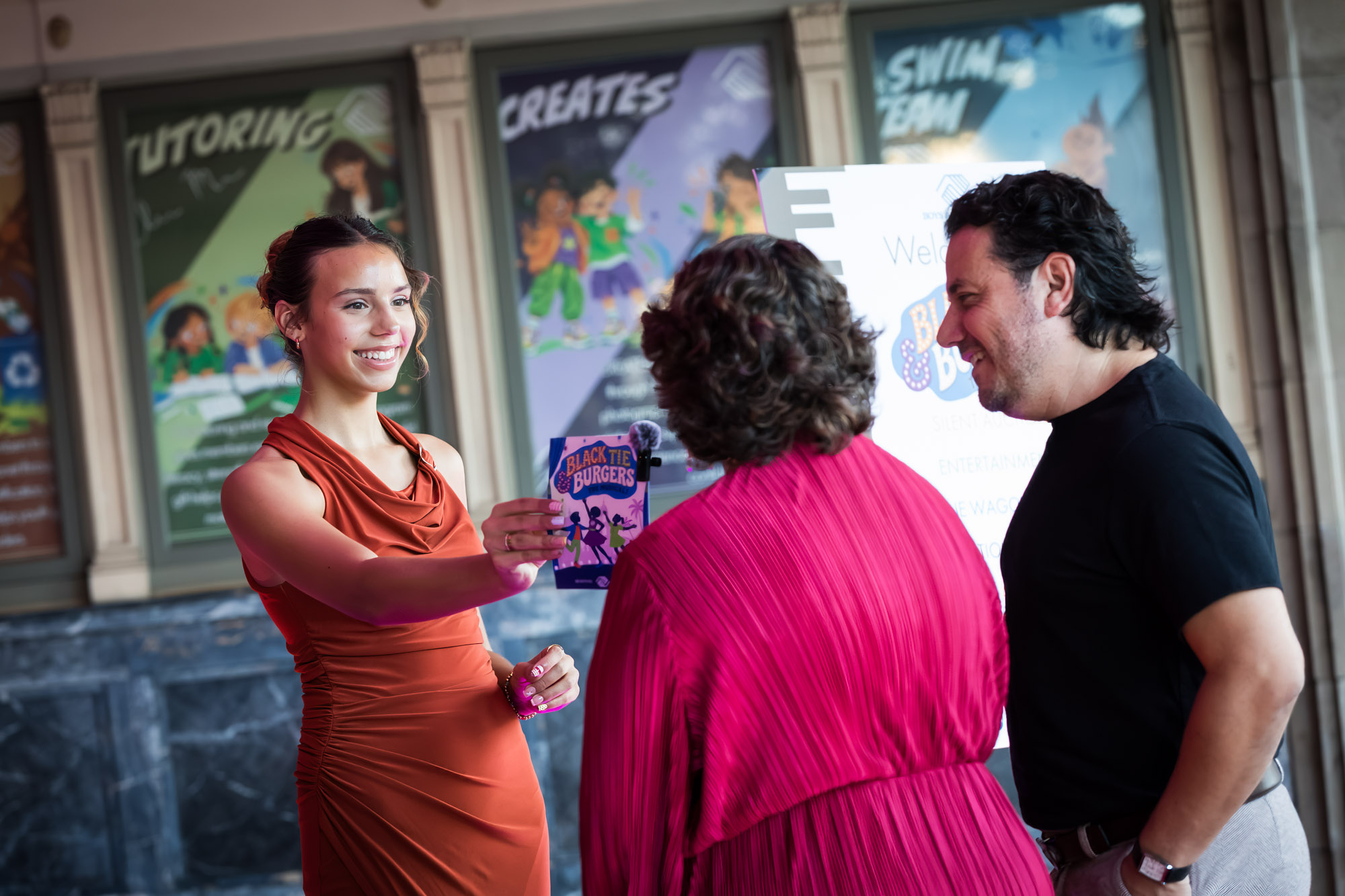 Raymond Theatre photos of a young greeter in an orange dress handing a program to arriving guests