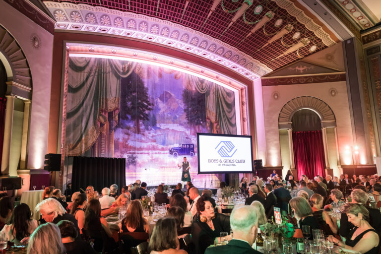 Raymond Theatre photos of a packed dining room watching a speaker in a kilt beneath the ornate painted curtain