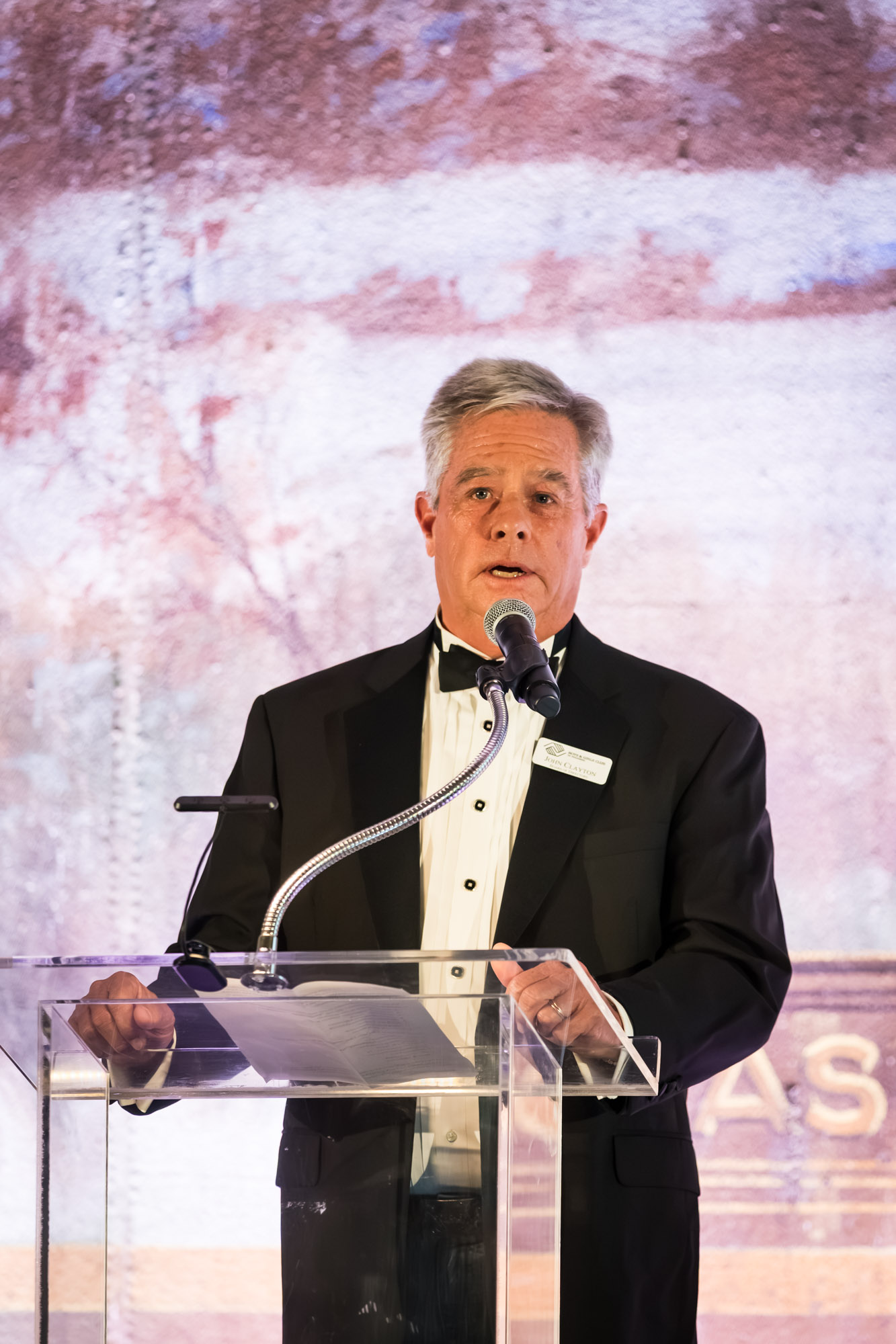 Los Angeles event photographer close-up of a speaker in a tuxedo at a clear podium with a gooseneck microphone