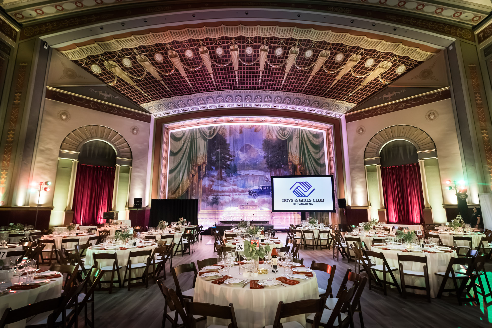 Raymond Theatre photos: wide view of the ornate coffered ceiling and painted curtain above round dinner tables
