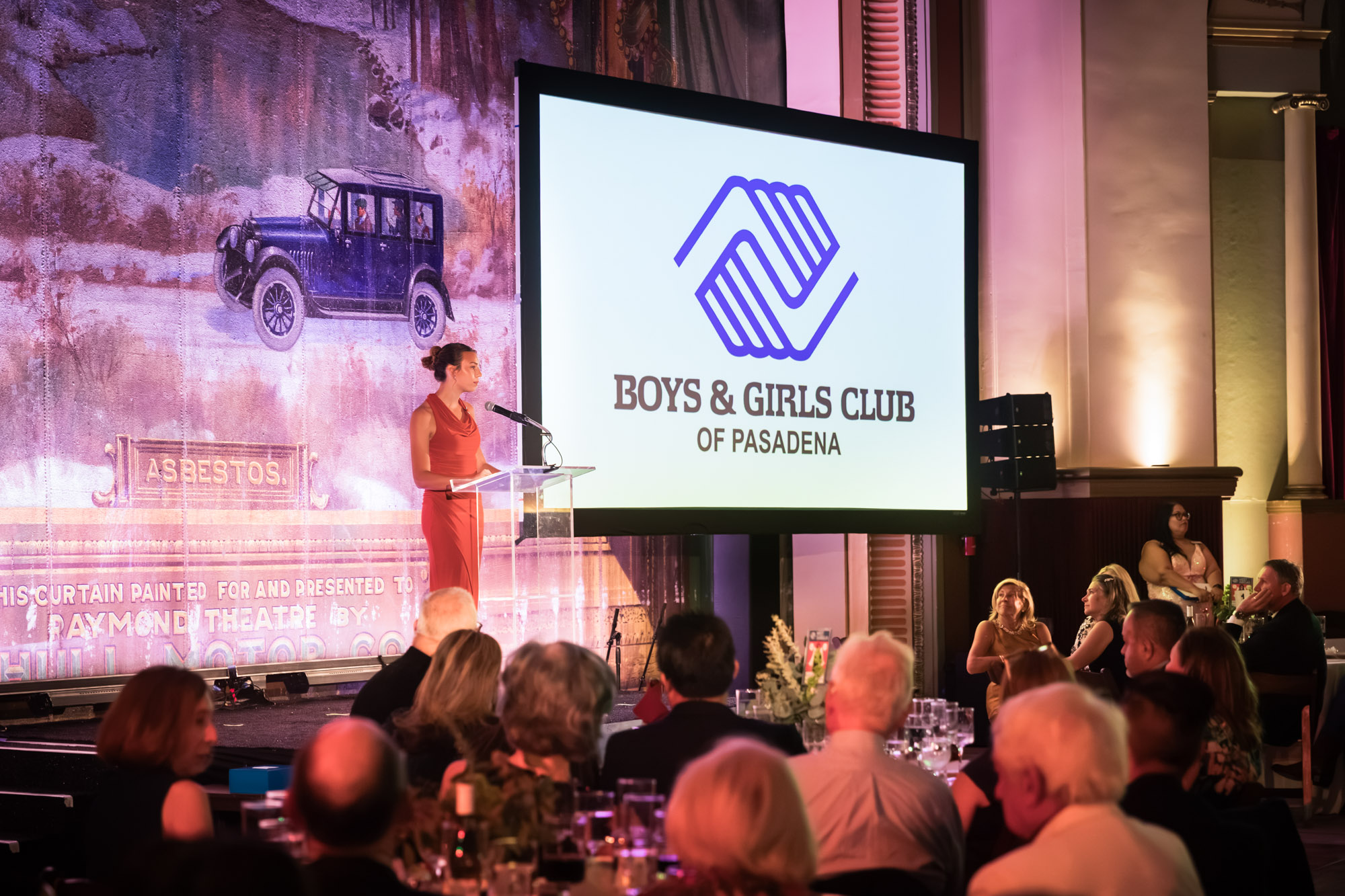 Raymond Theatre photos of a speaker at the podium beside the Boys & Girls Club logo, with guests in the foreground