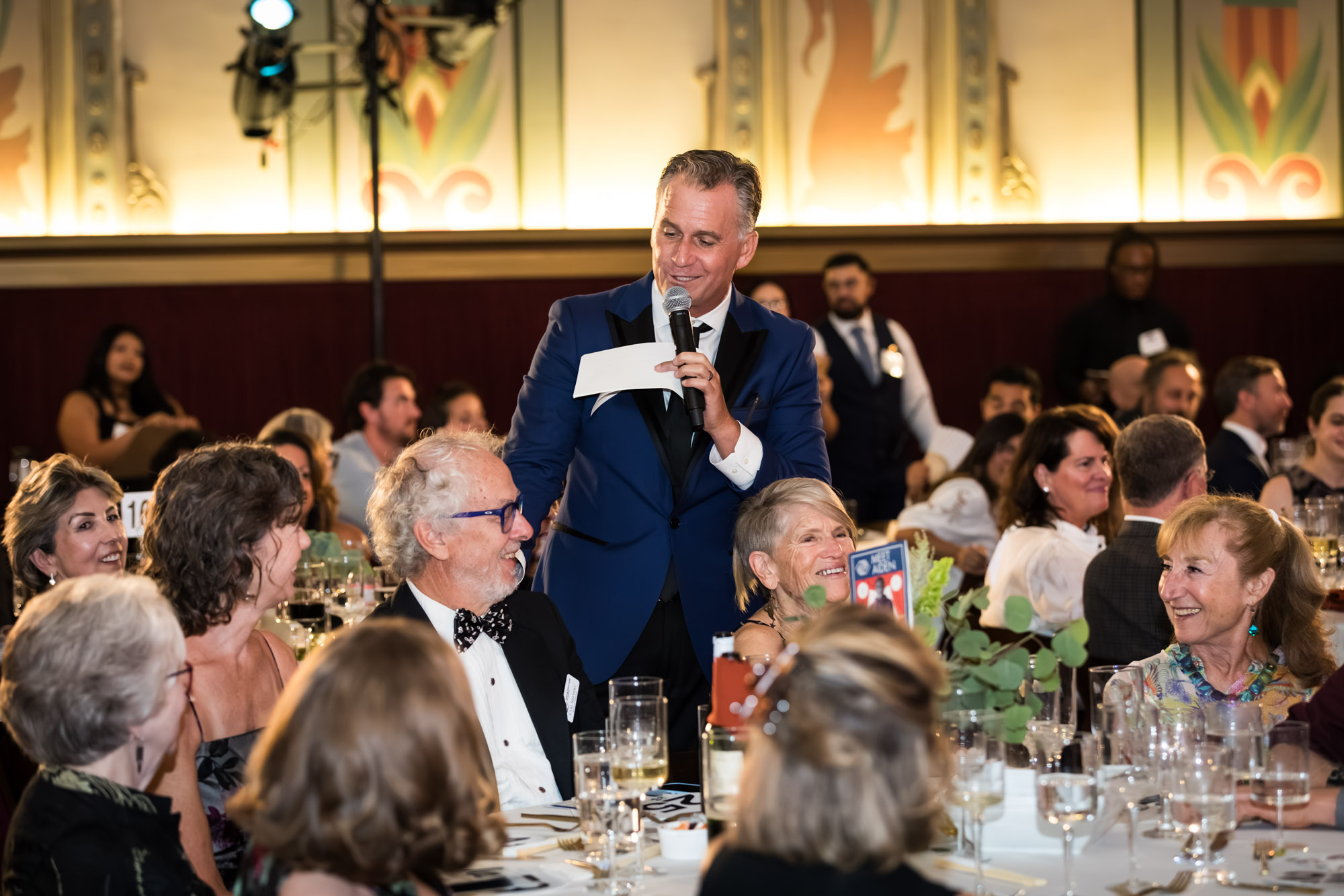 Los Angeles event photographer image of a speaker in a blue jacket chatting with smiling guests at a dinner table