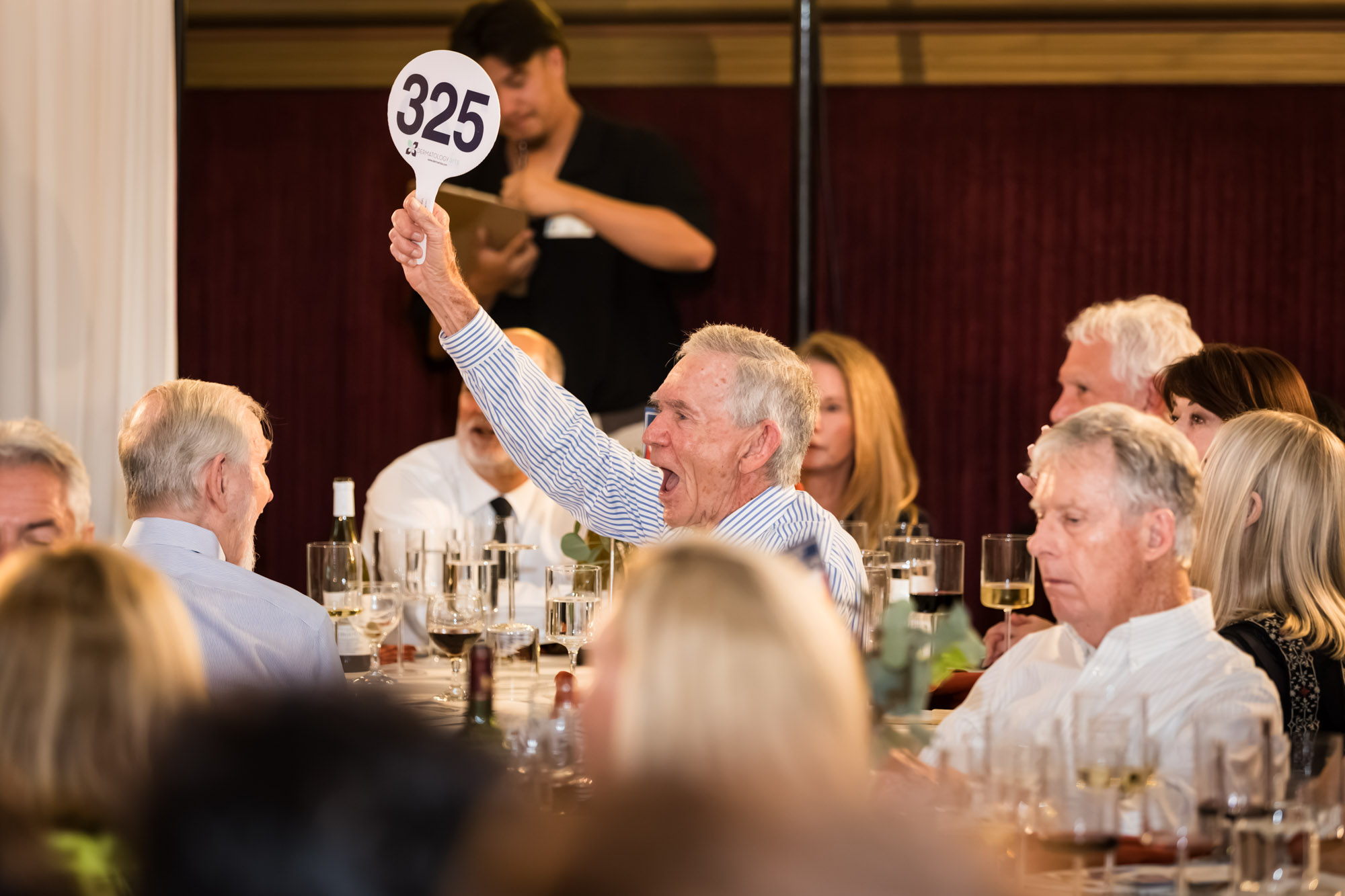 Raymond Theatre photos of a guest in a striped shirt raising a bidder paddle with an excited cheer