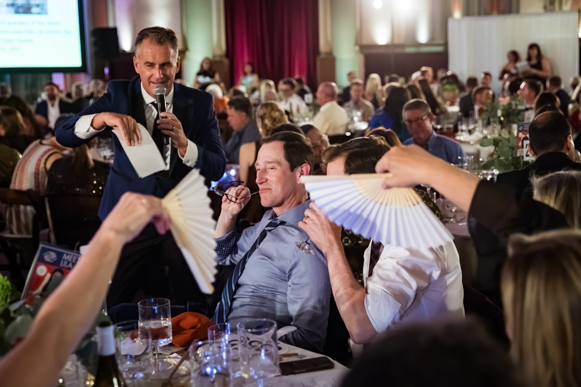Los Angeles event photographer shot of a speaker joking with a seated guest as nearby guests hold paper fans