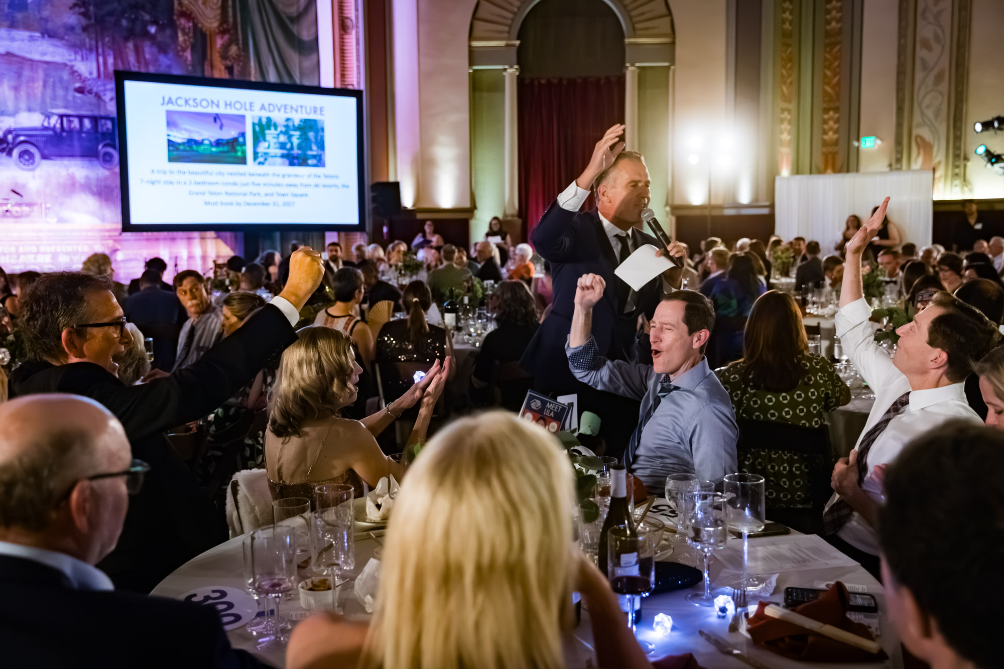 Raymond Theatre photos of guests cheering with raised fists and arms as a speaker works the room with a microphone