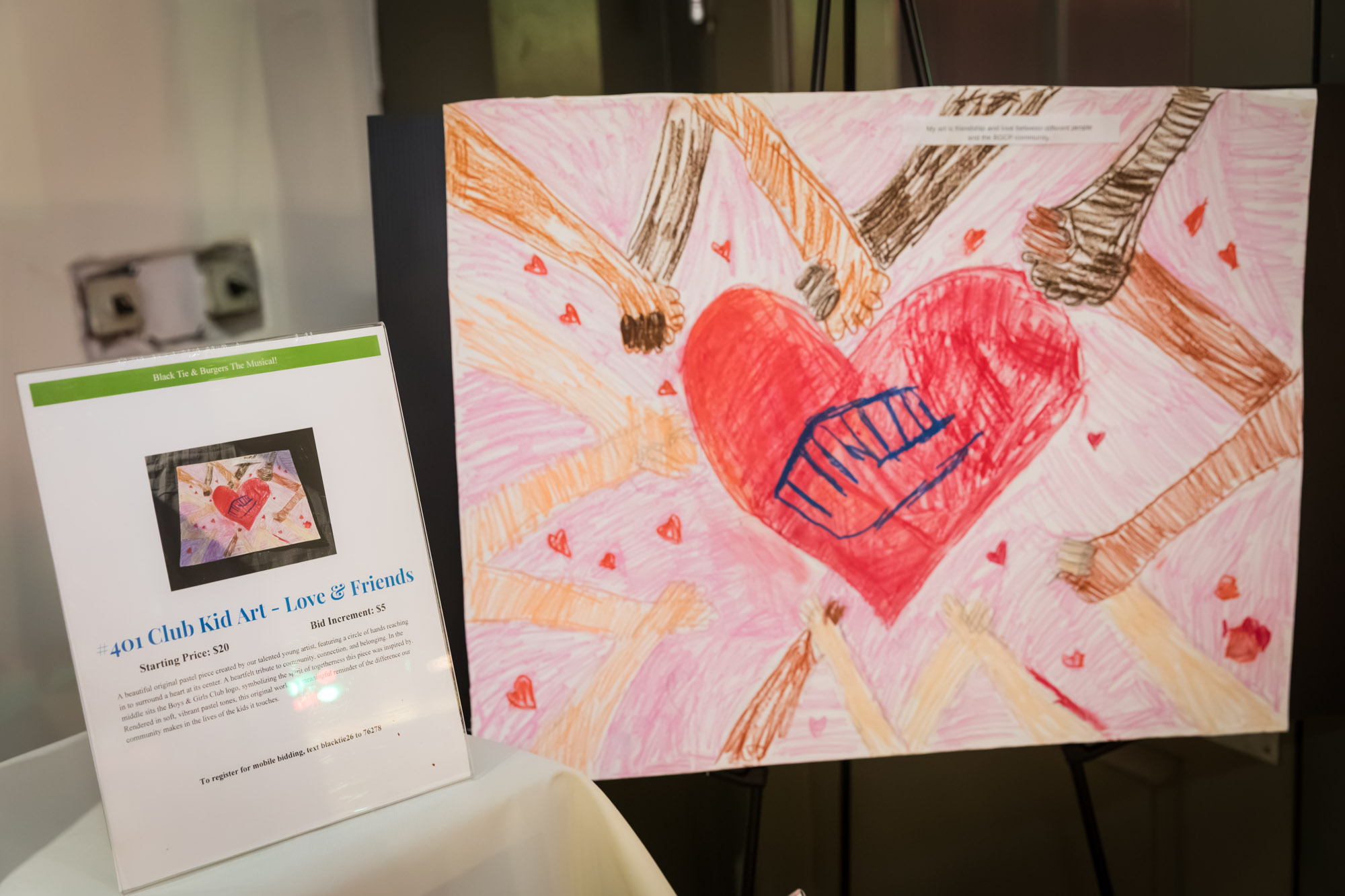 Raymond Theatre photos of Club kid art of hands circling a heart, shown with an auction bid sign
