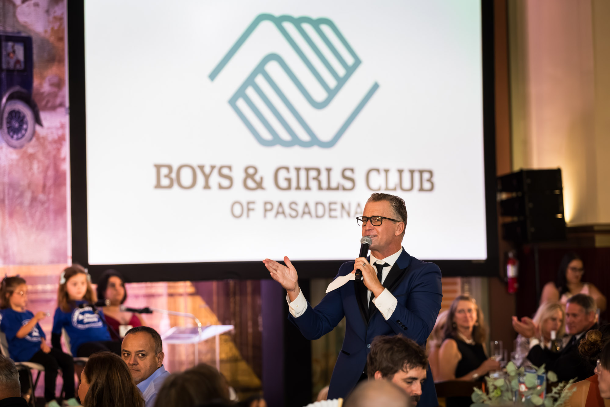 Raymond Theatre photos of a speaker in a blue jacket gesturing in front of the Boys & Girls Club logo screen