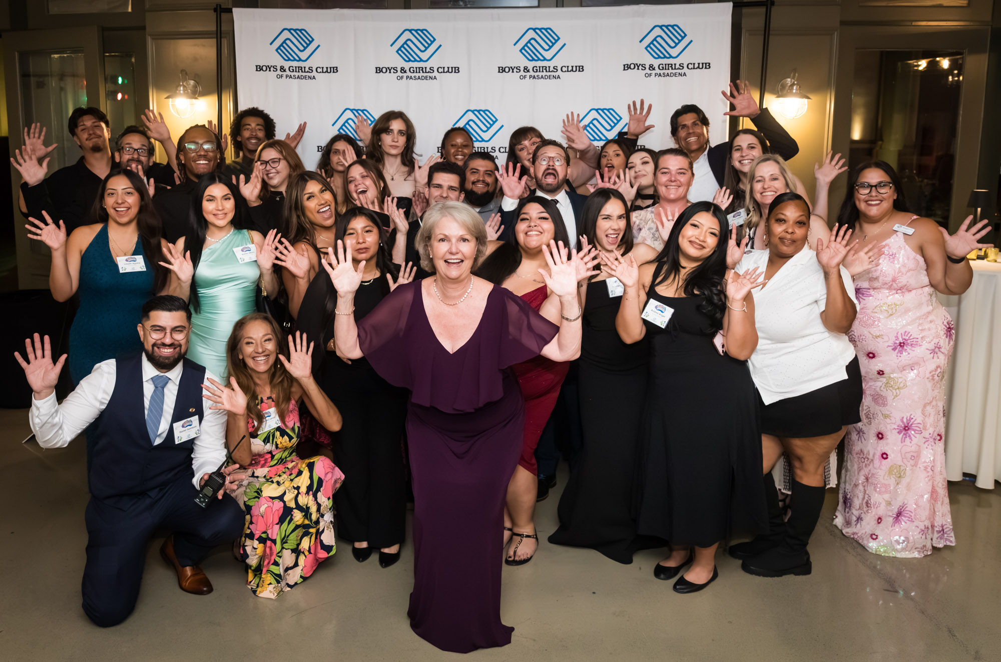 Los Angeles event photographer group photo of smiling guests in formal wear waving in front of the club backdrop